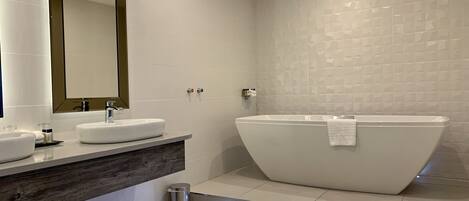 A modern bathroom with a freestanding bathtub, a large mirror, and a vanity with a sink and towel rack.