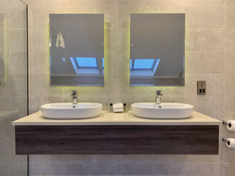 Un baño moderno con dos lavamanos, un espejo grande y un tragaluz.
