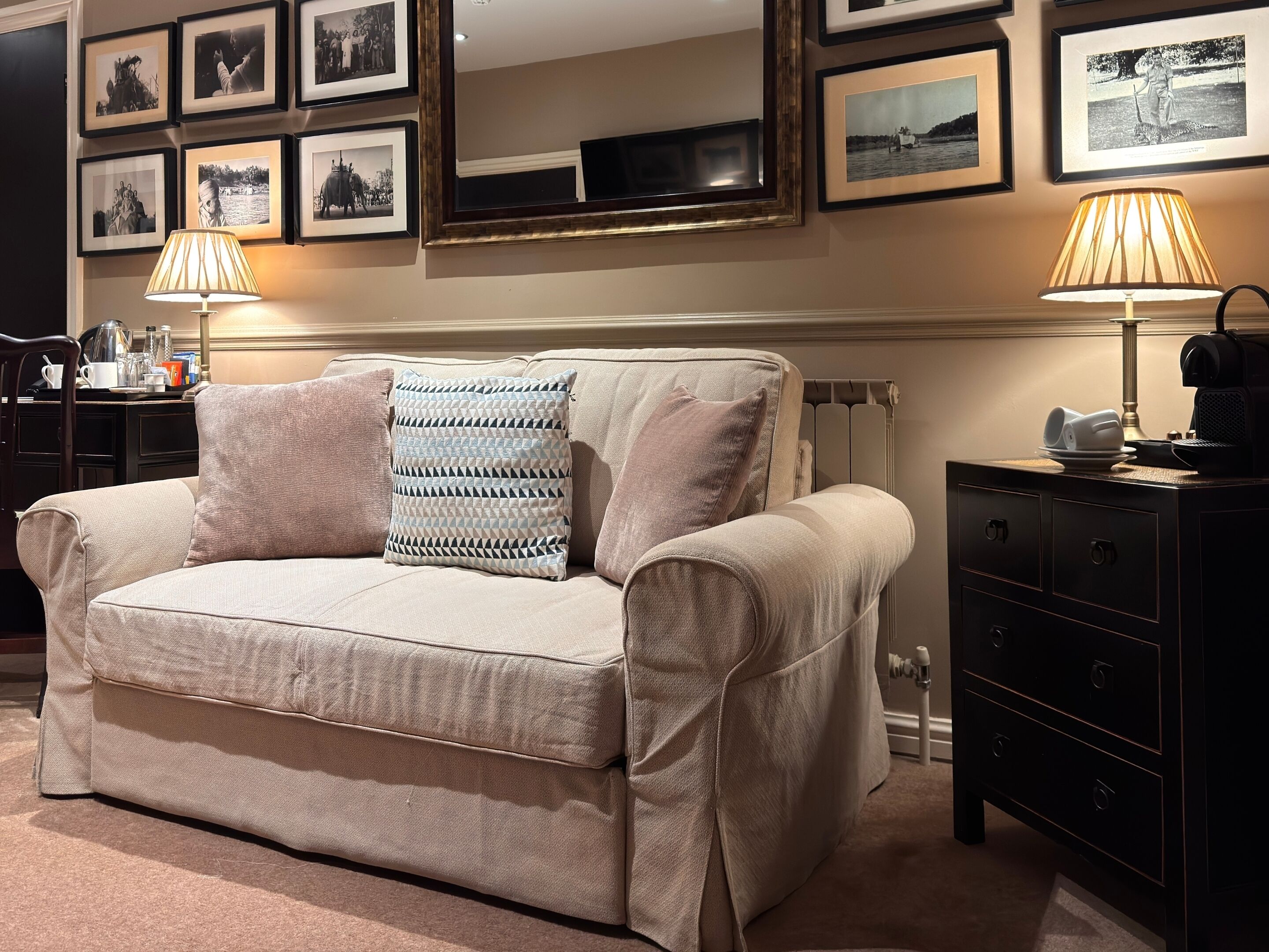 A beige sofa with patterned cushions, a black side table with a lamp, and a wall with framed black-and-white photographs.