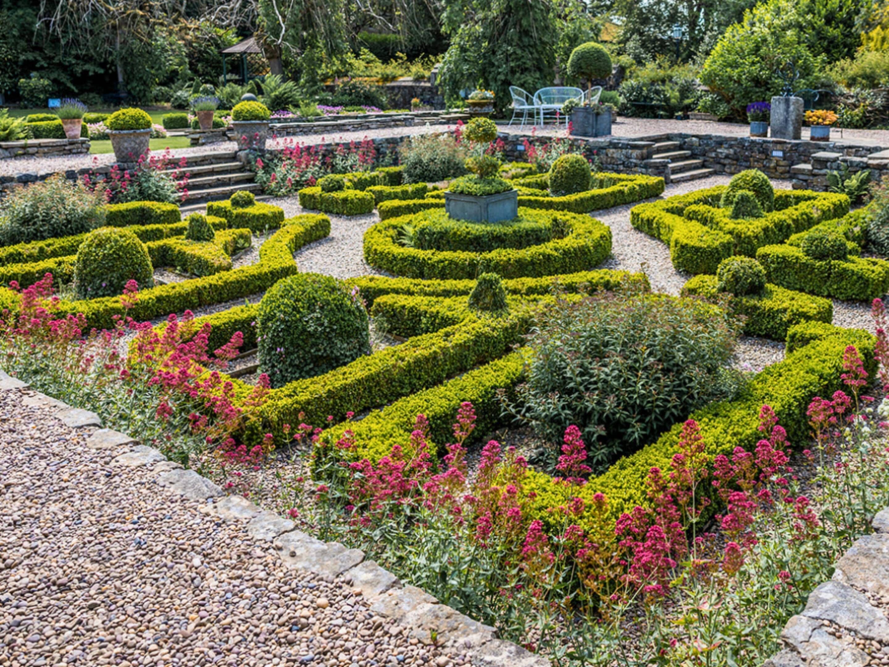 Un jardín meticulosamente cuidado con setos geométricos y una variedad de plantas en flor.