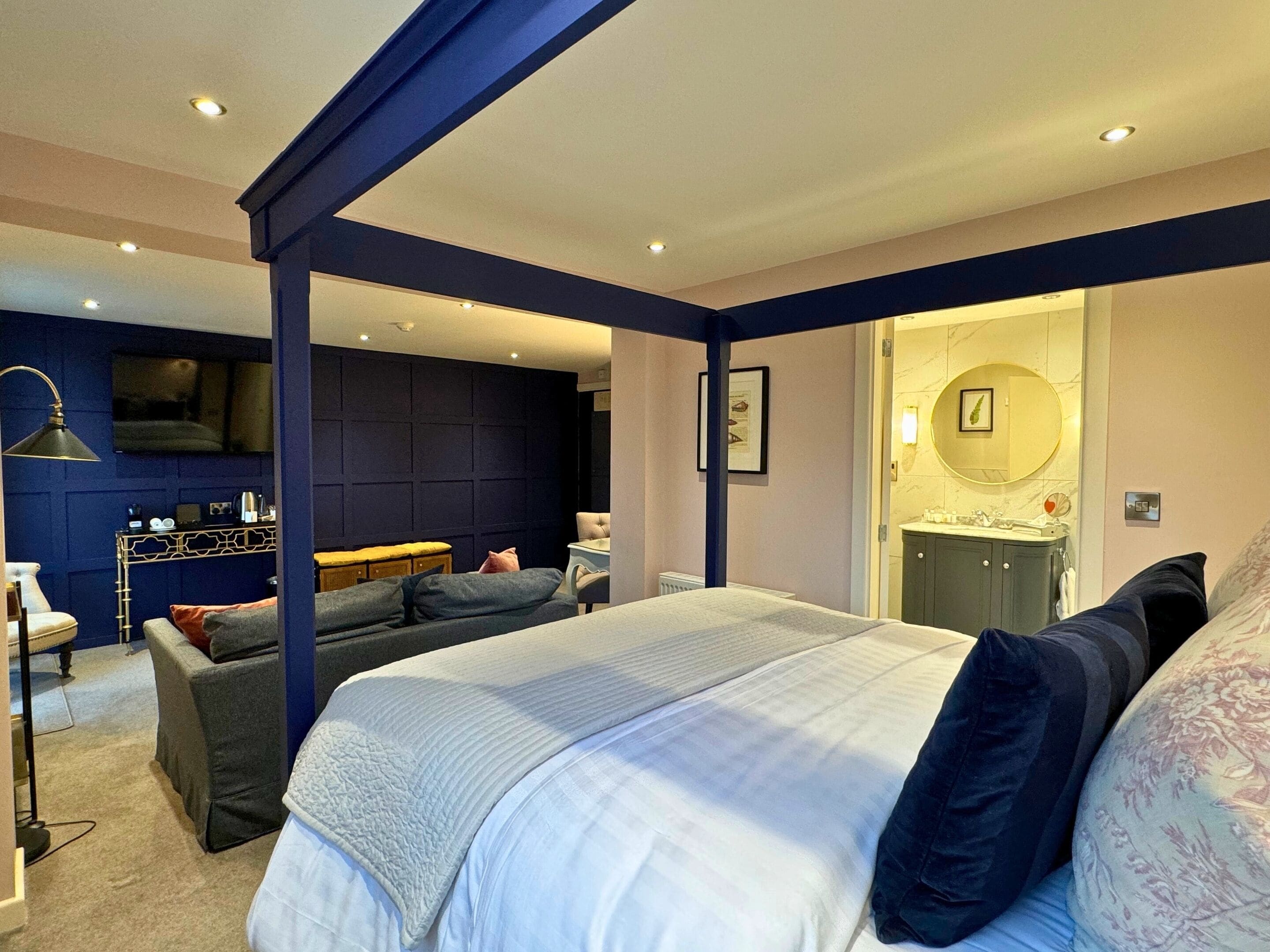 Une chambre moderne avec un grand lit, un canapé, un bureau et une salle de bain visible à travers une porte ouverte.