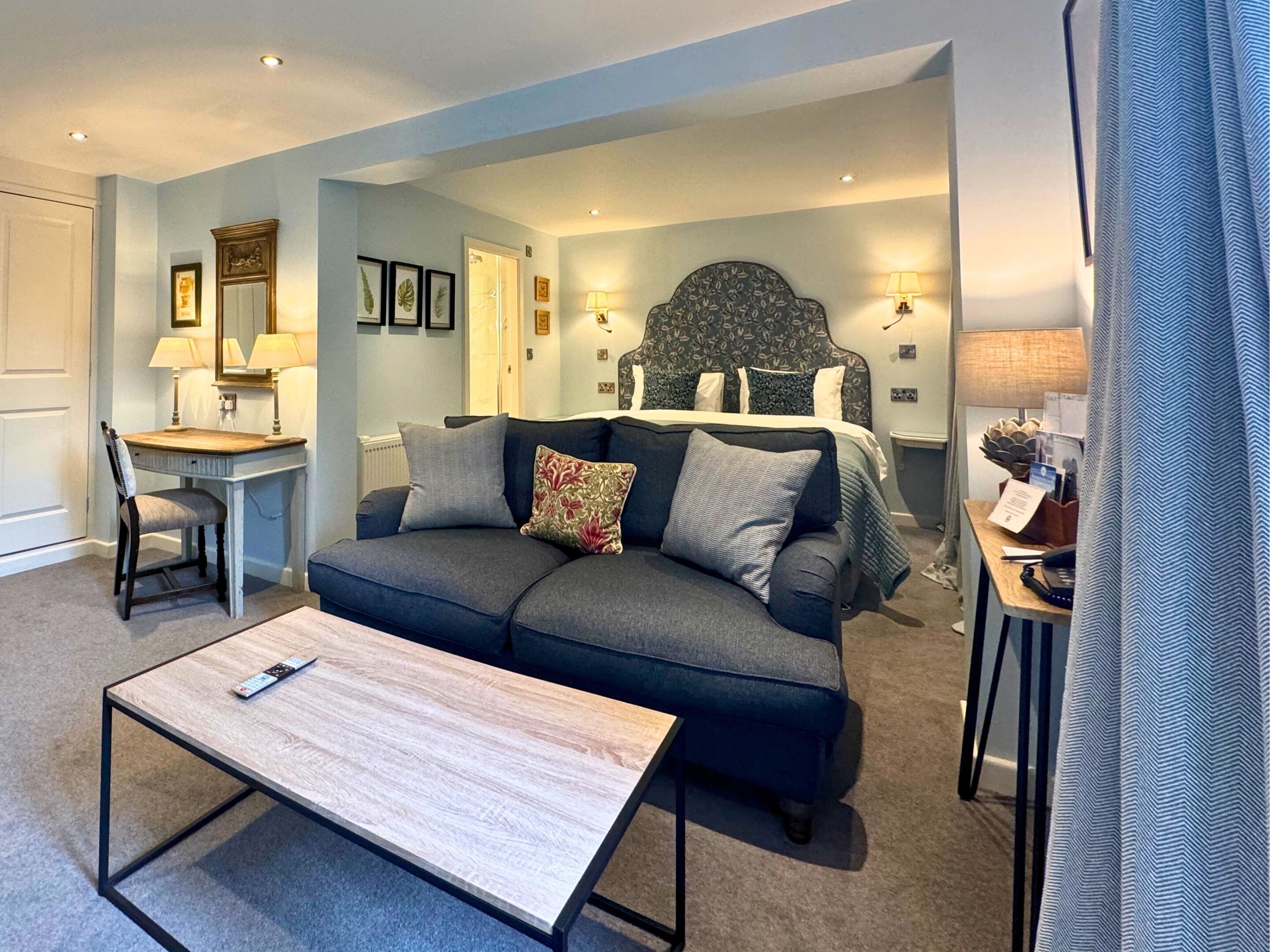 A modern living room with a sofa, a coffee table, a desk, and a bed with a headboard.