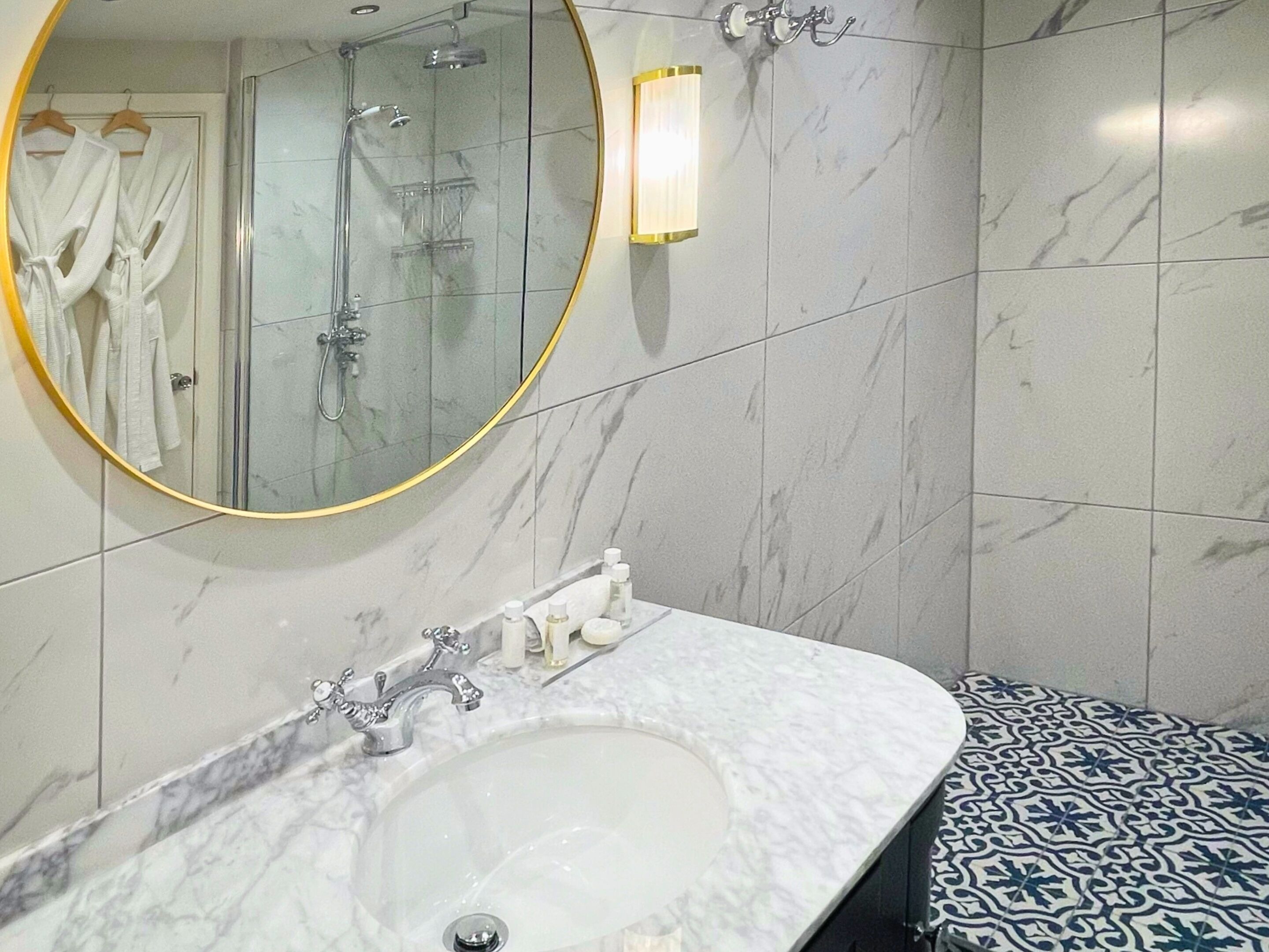 A bathroom with a marble sink, a shower, and a mirror with a gold frame.