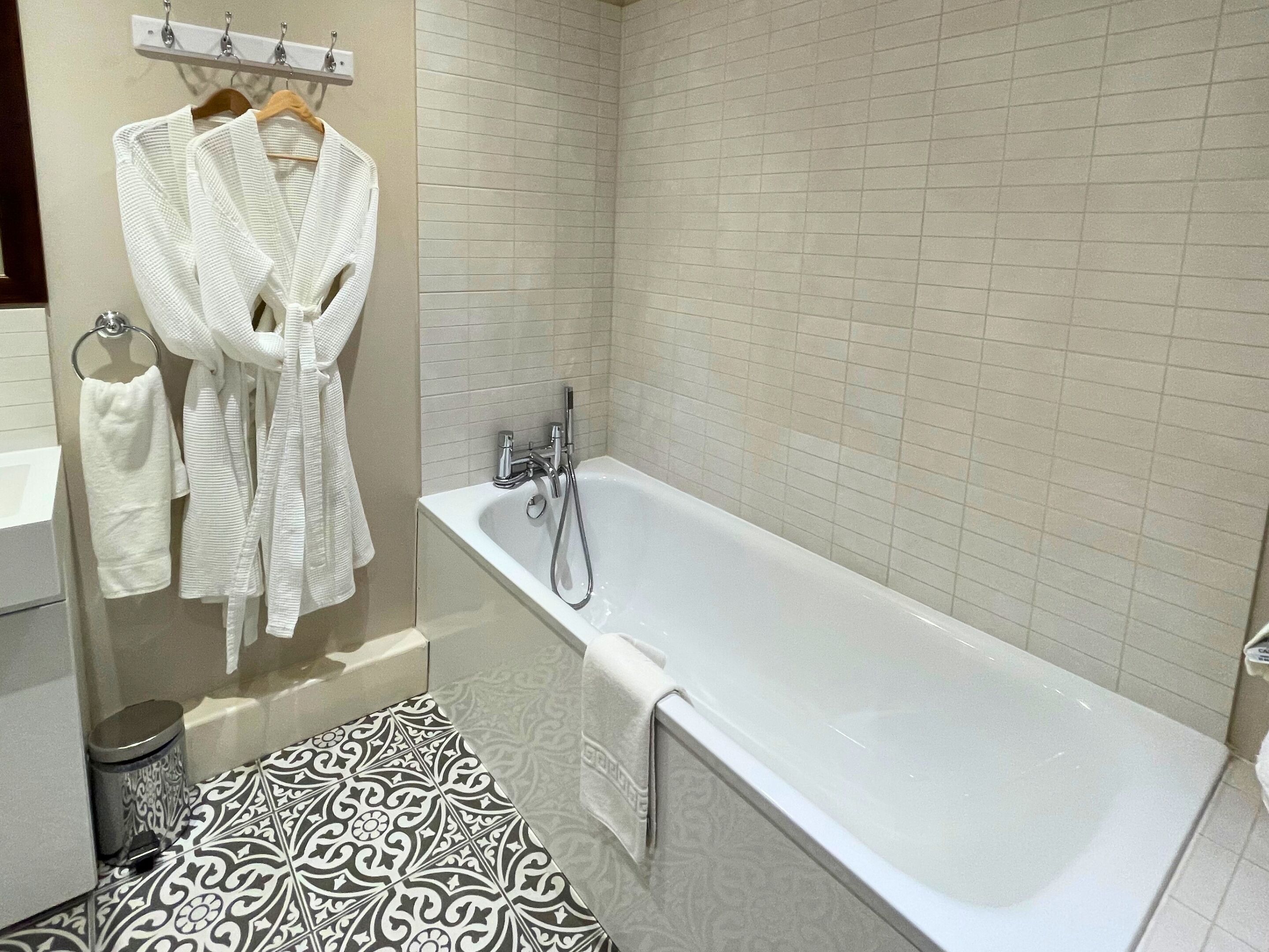 Un baño moderno con bañera, un perchero con batas y baldosas de suelo estampadas.