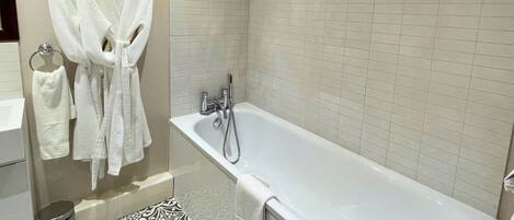 A modern bathroom with a bathtub, a towel rack with robes, and patterned floor tiles.
