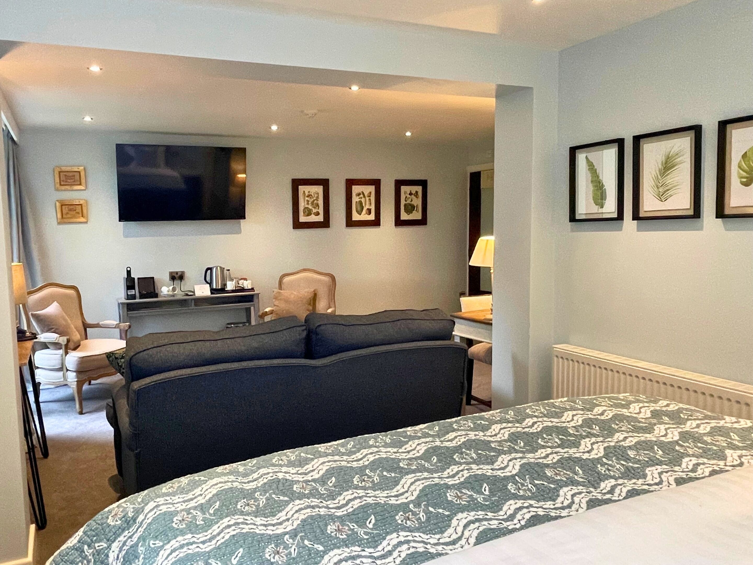 A hotel room with a large bed, a TV, a desk with a lamp, and framed pictures on the wall.