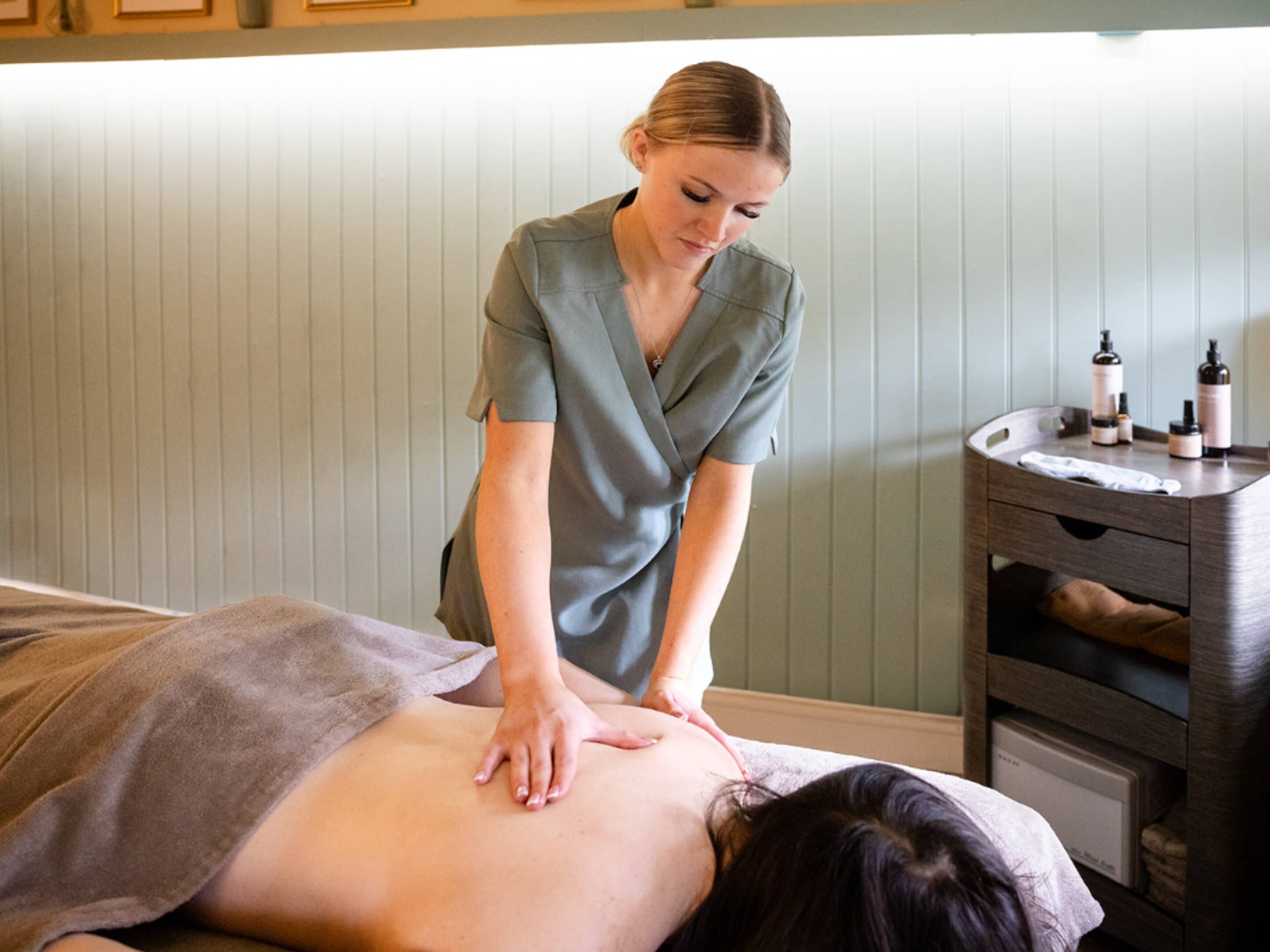 A massage therapy session in a room with a wooden cabinet and a small table with bottles.