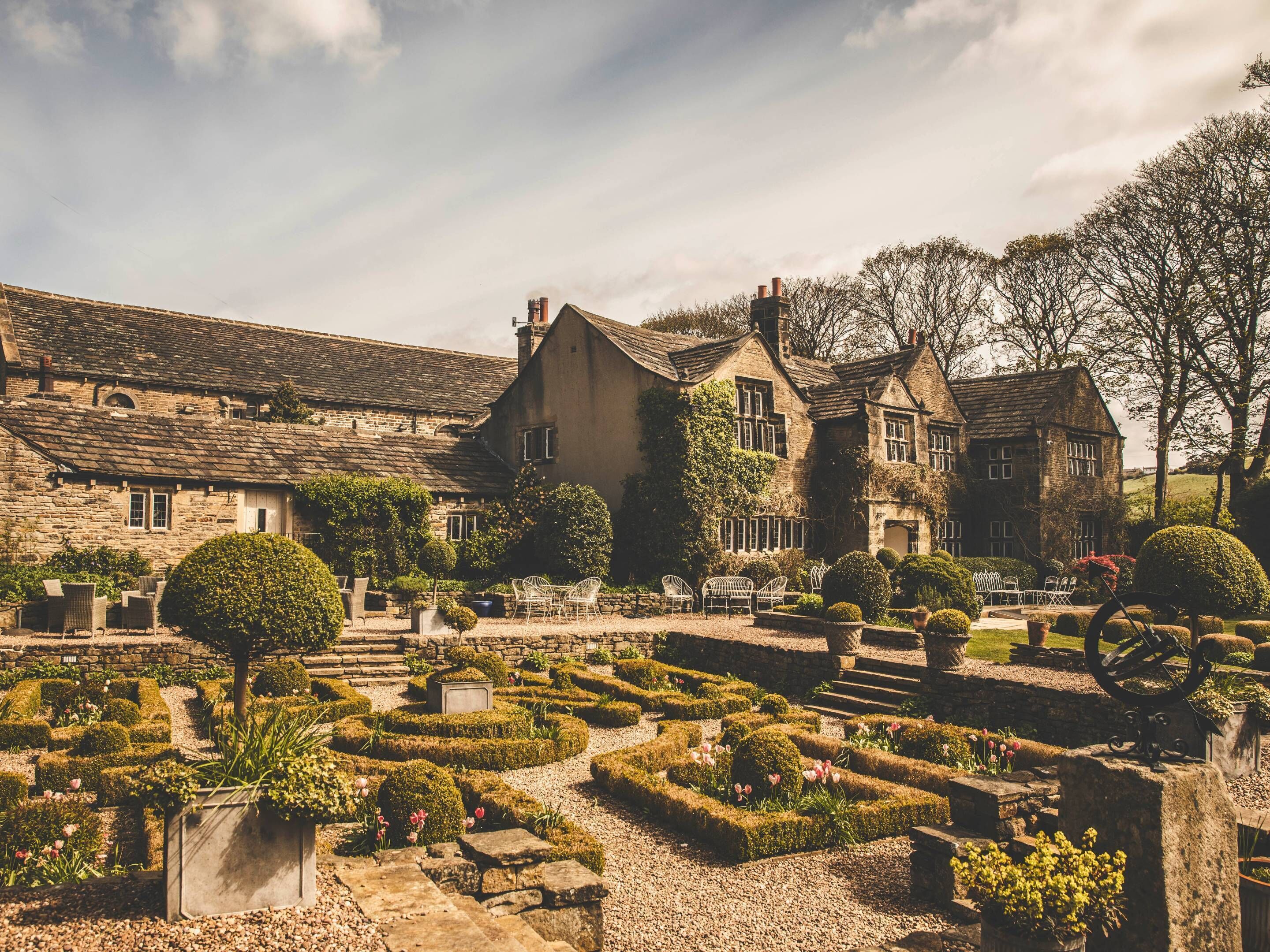 A traditional stone building with a garden featuring hedges and a central circular lawn.