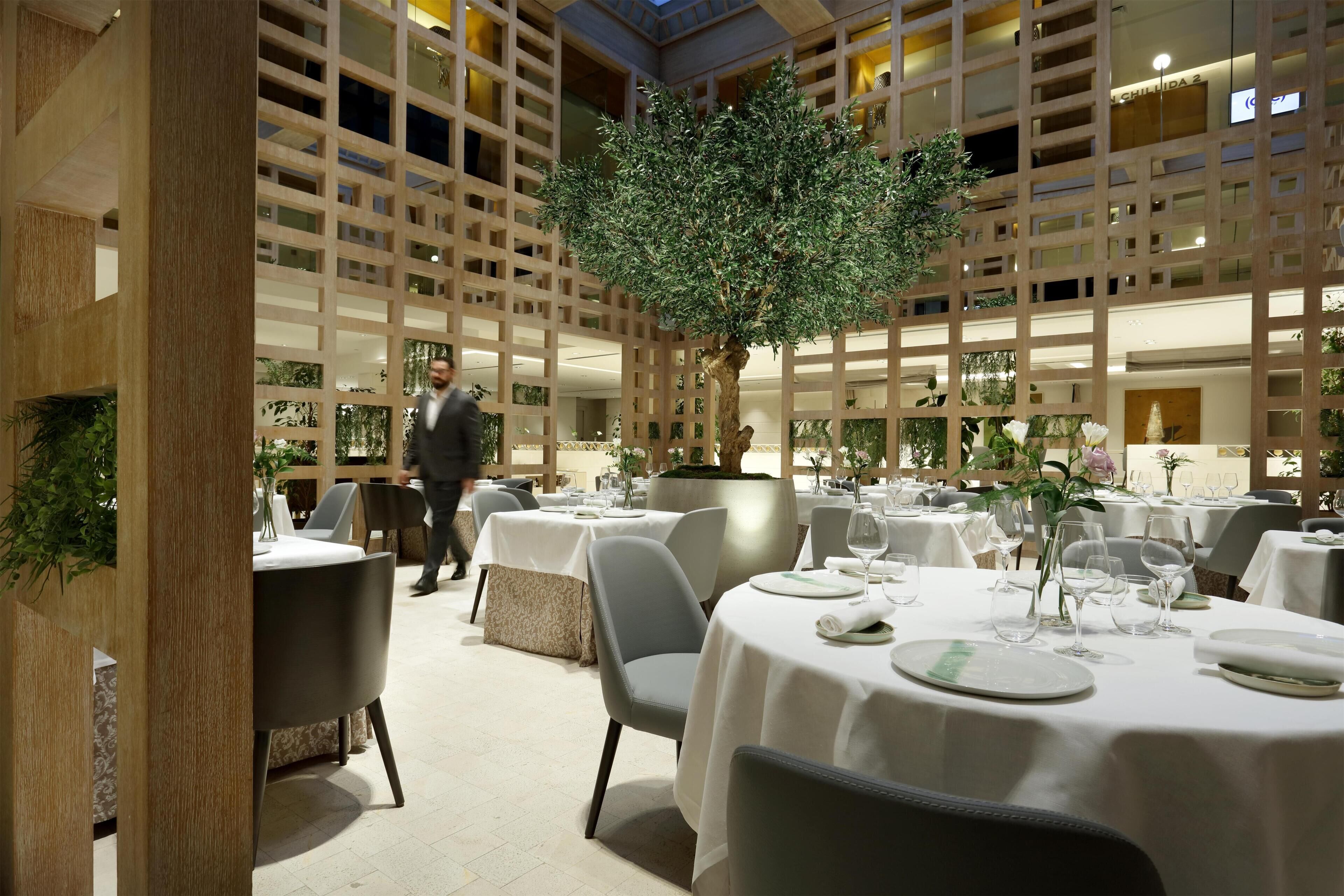 A restaurant with multiple tables, a central tree, and a modern interior design.