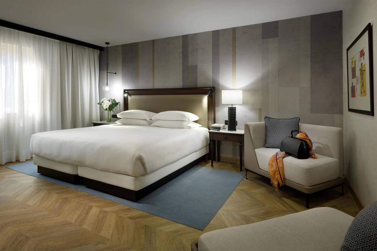 A hotel room with a large bed, a desk, a chair, and a sofa.