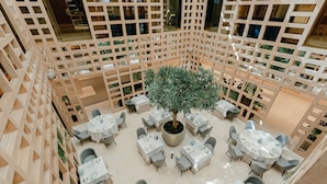 A multi-level atrium with a central tree, surrounded by multiple dining tables and chairs. - Hyatt Regency Hesperia Madrid (Madrid)