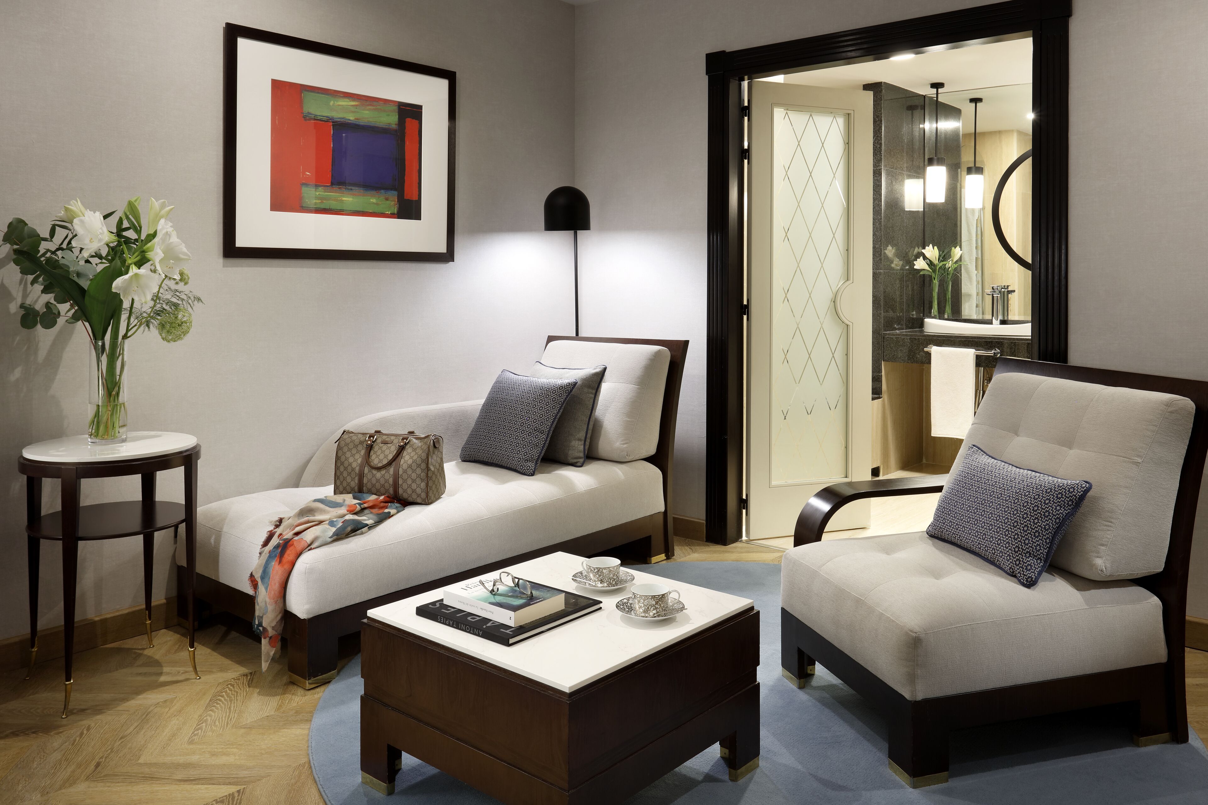 Una sala de estar moderna con sofá, sillón, mesa de centro y un cuadro abstracto enmarcado.