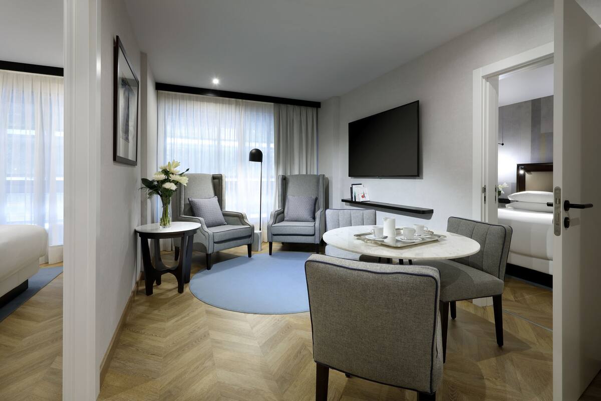 A modern hotel room with a seating area, a flat-screen TV, and a bed.