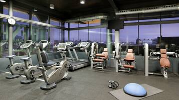 Un gimnasio con máquinas de cardio, equipo de entrenamiento de fuerza y una pelota de ejercicio azul.