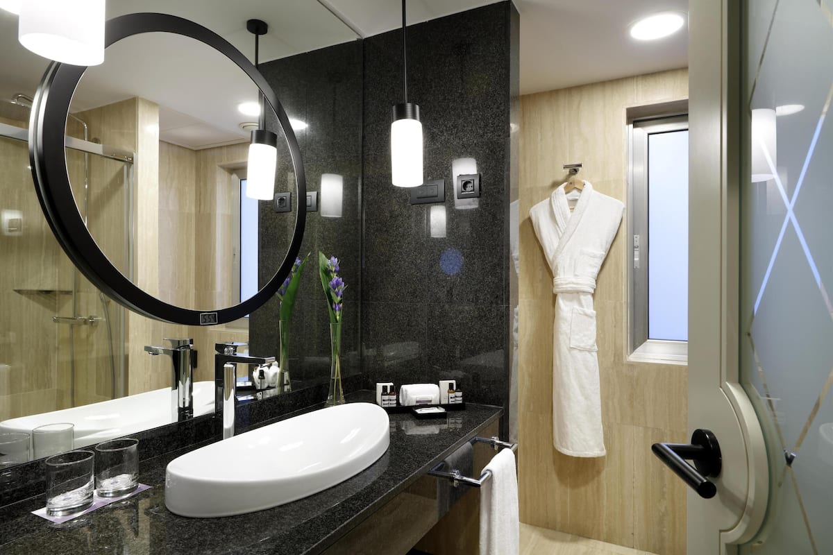 A modern bathroom with a large oval sink, a round mirror, and a robe hanging on the door.