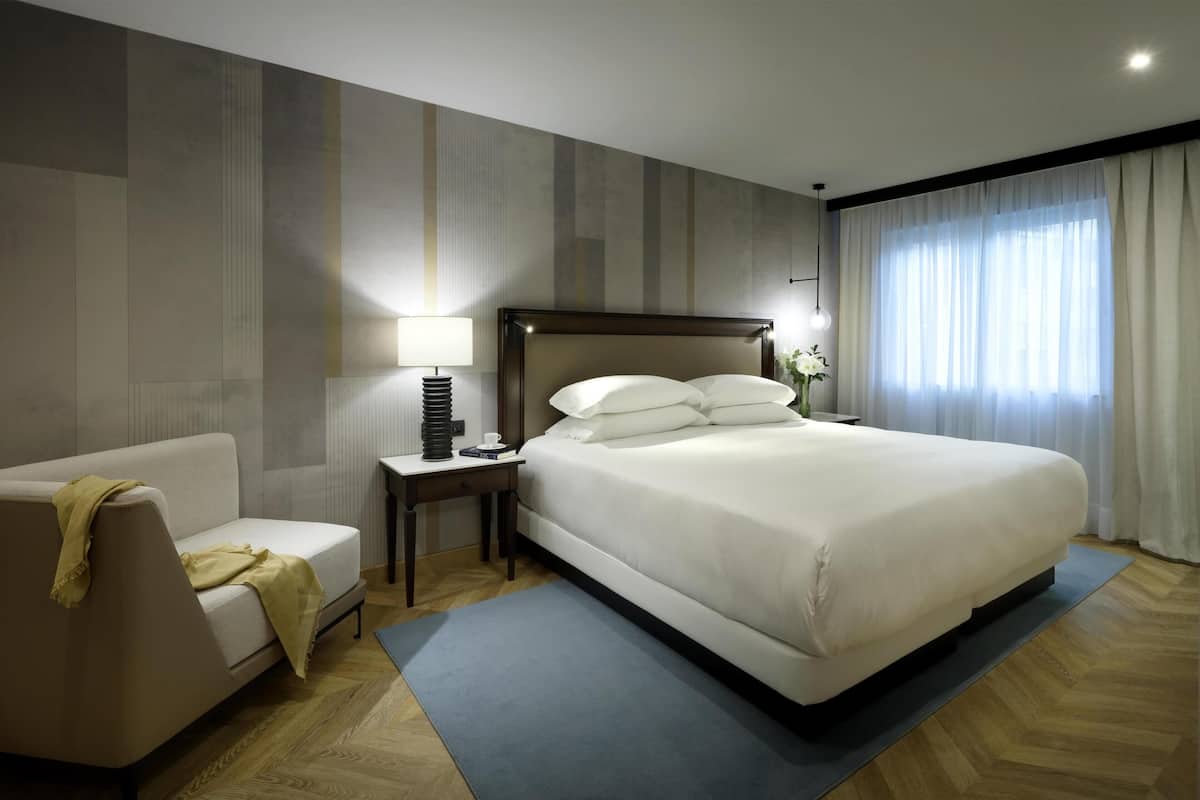 A hotel room with a bed, a sofa, a nightstand, a lamp, and a window with curtains.