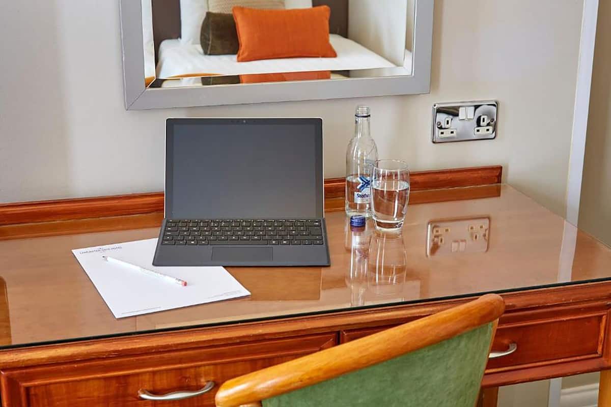 A hotel room with a wooden desk, a laptop, a bottle of water, and a glass.