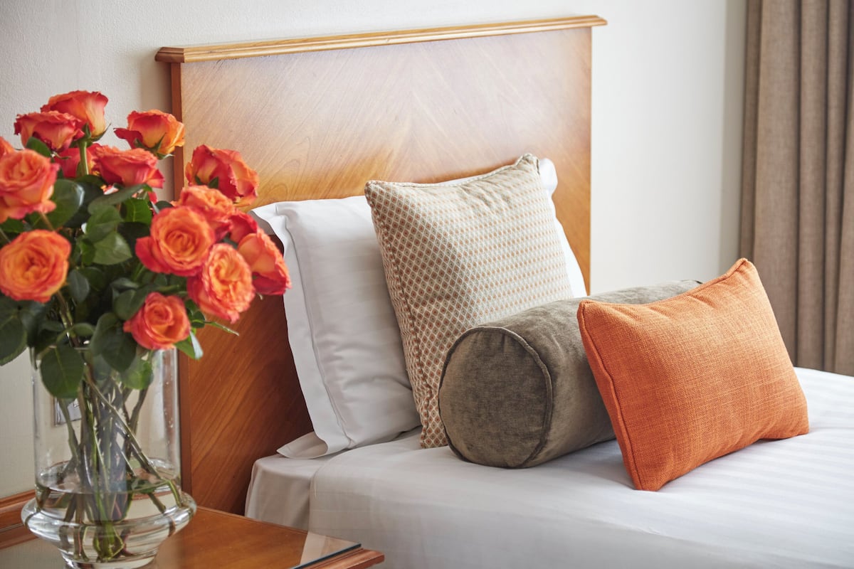 A neatly made bed with a wooden headboard, a vase of roses, and a variety of pillows.