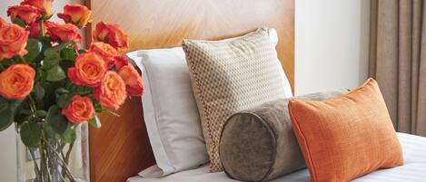A bed with a wooden headboard, white bedding, and three pillows in different textures and colors.