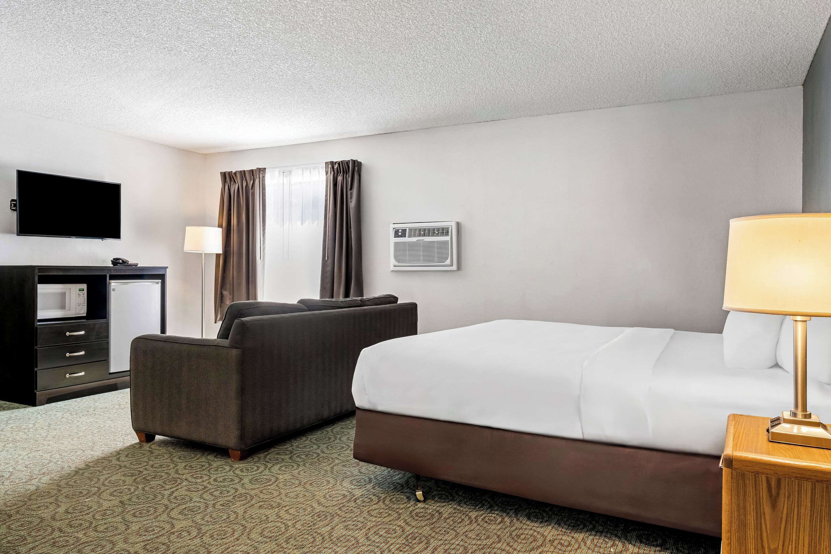 Una habitación de hotel con cama, escritorio con televisor, silla y unidad de aire acondicionado.