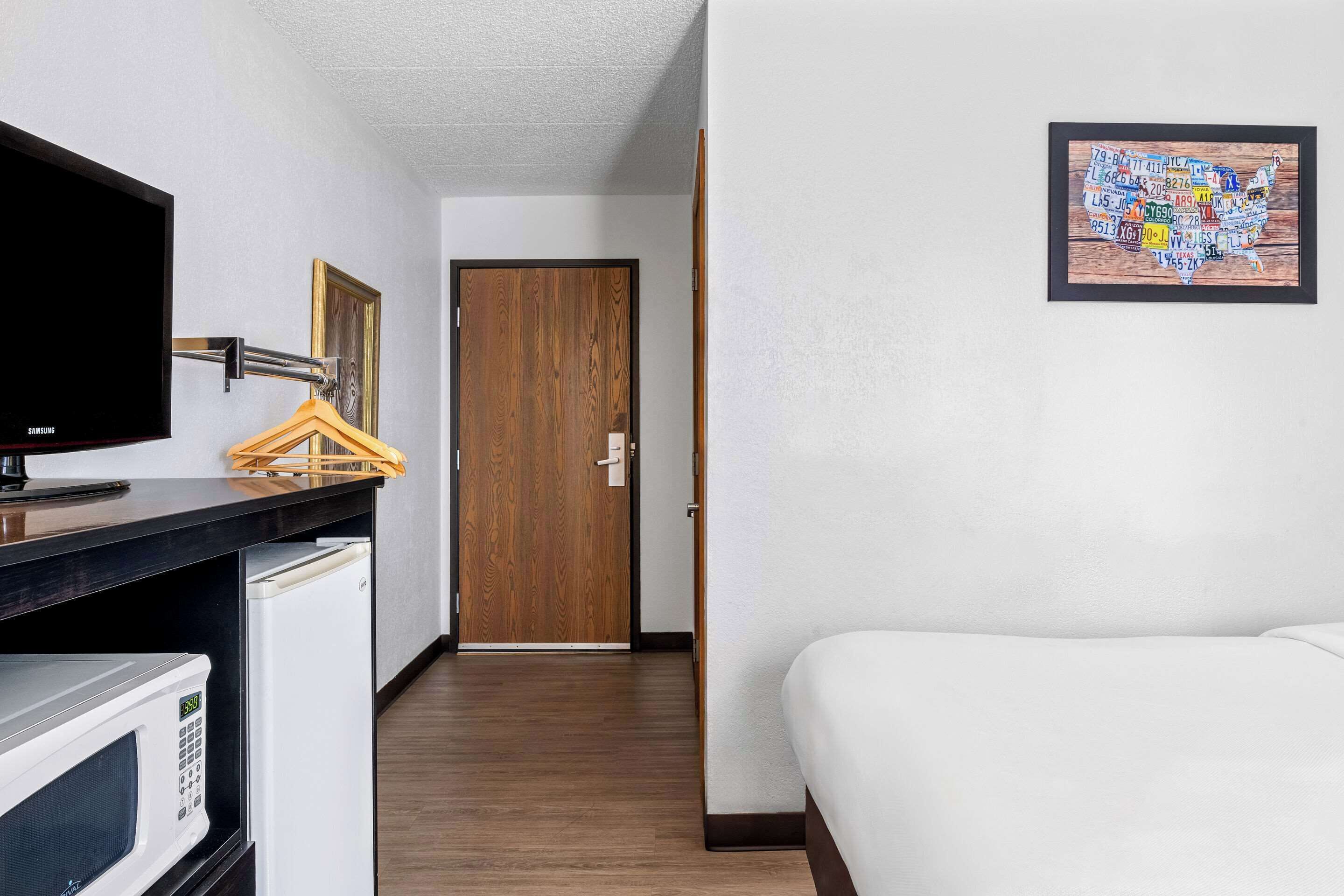 A hotel room with a bed, a TV, a microwave, and a wooden door.