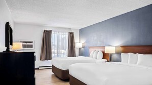 Ett hotellrum med två sängar, ett skrivbord, en lampa och ett fönster med gardiner.