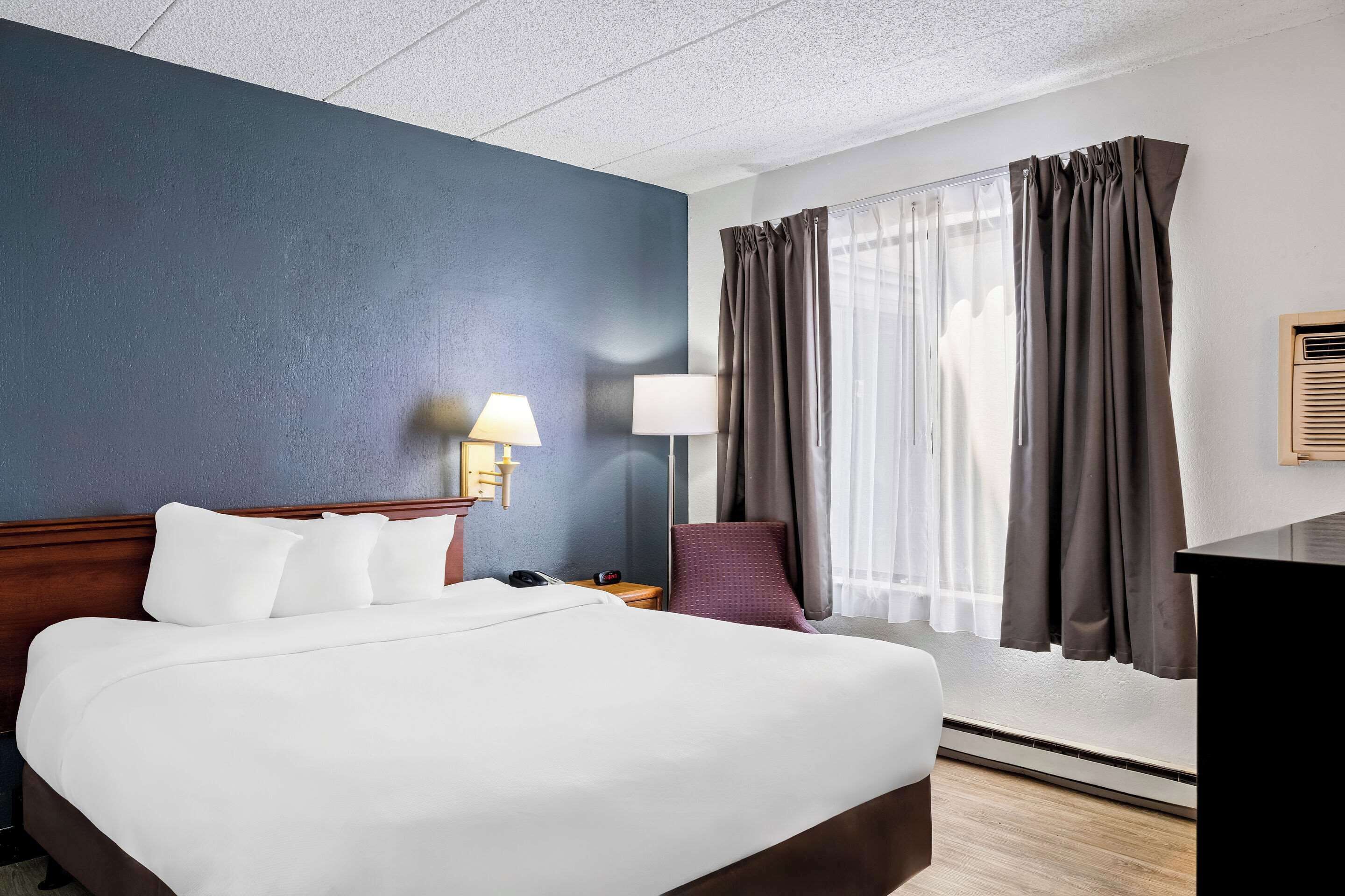 Une chambre d’hôtel avec un grand lit, un bureau, une chaise, une lampe et une fenêtre avec des rideaux.
