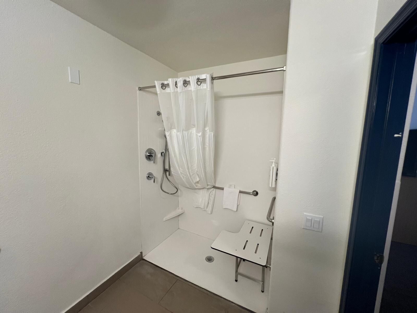 Een kleine, witte badkamer met een douche, een handdoekhouder en een klein tafeltje.