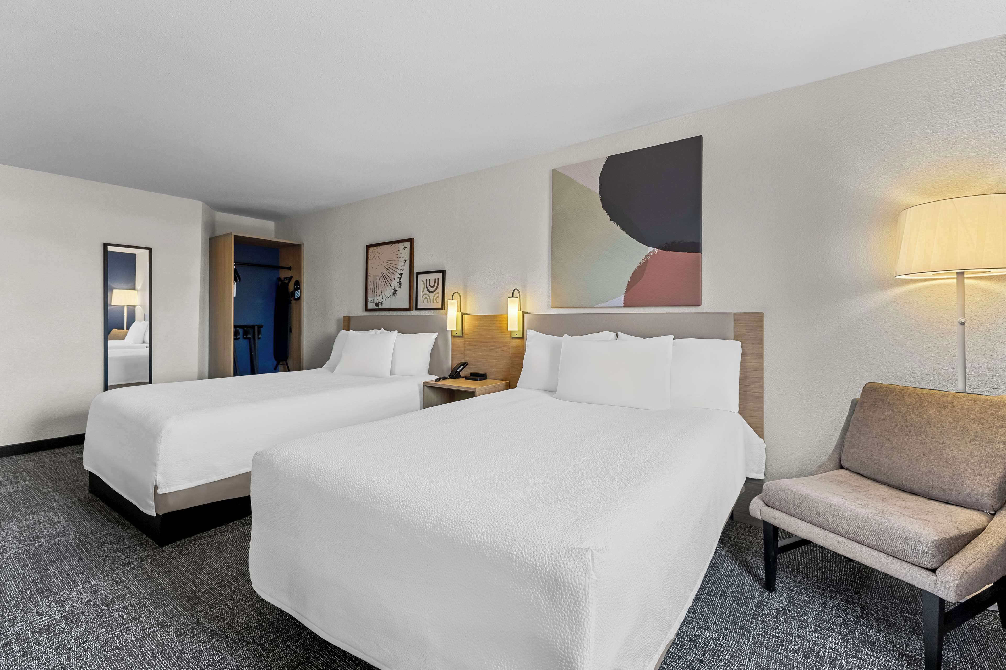 Una habitación de hotel con dos camas, una silla, un escritorio y una lámpara.