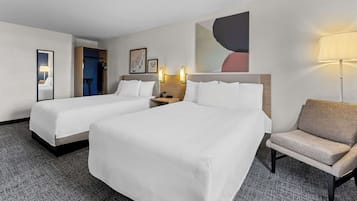 Una habitación de hotel con dos camas, una silla, un escritorio y una lámpara.