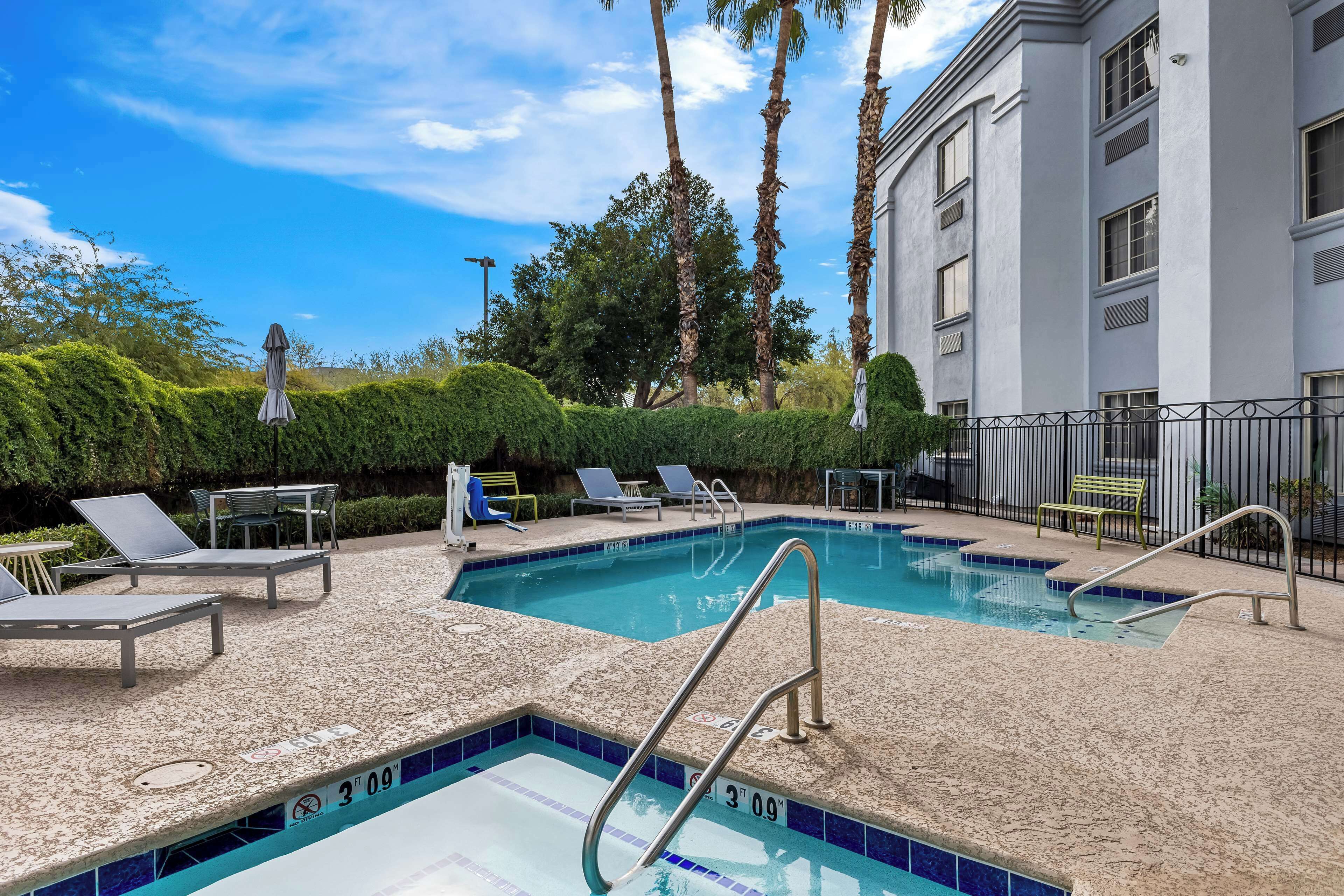 A swimming pool with a tiled deck, lounge chairs, and a bench.
