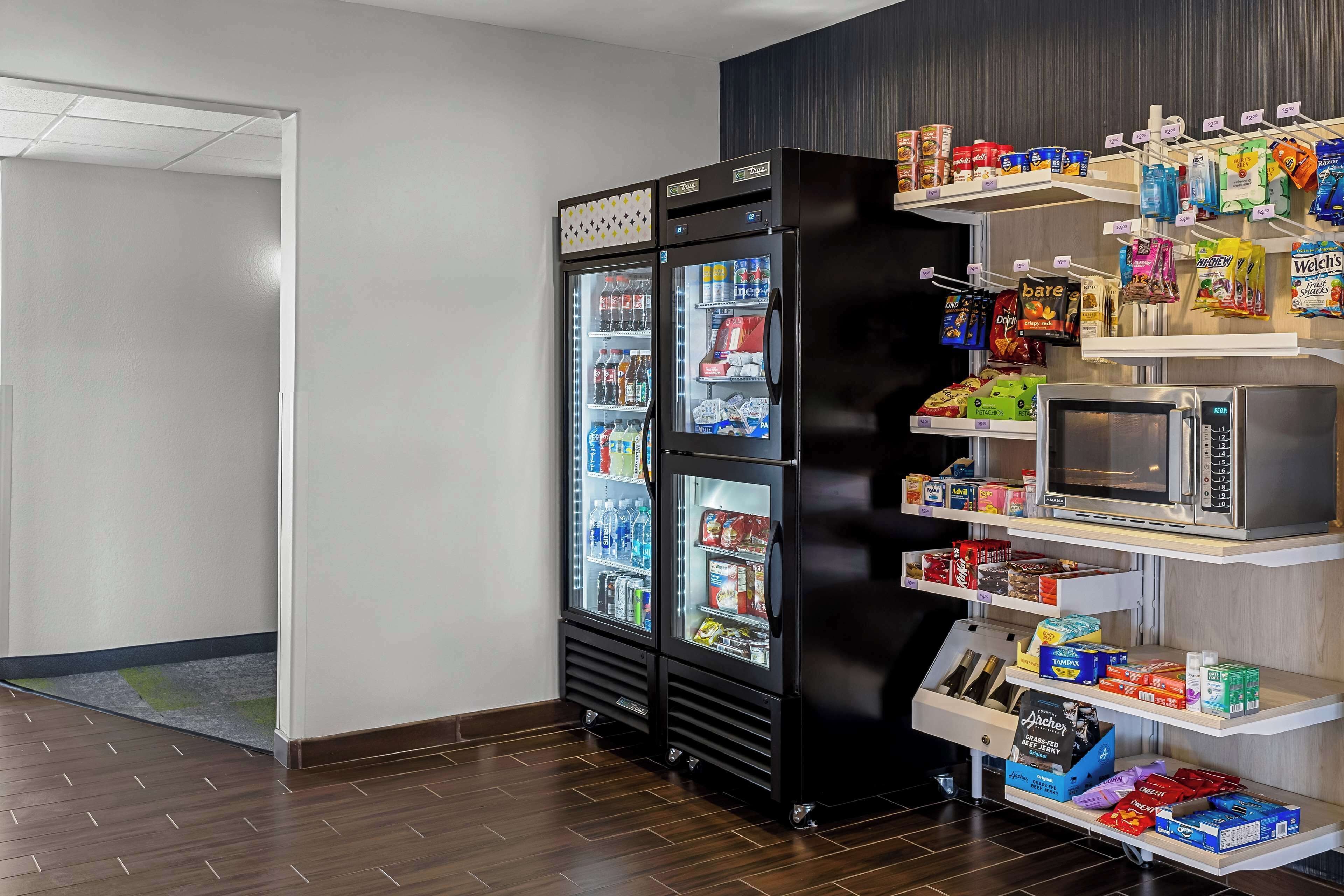 A hotel room with a minibar, a microwave, and shelves stocked with snacks and beverages.