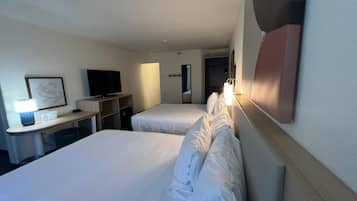 A hotel room with two beds, a desk with a lamp, a television, and a mirror.