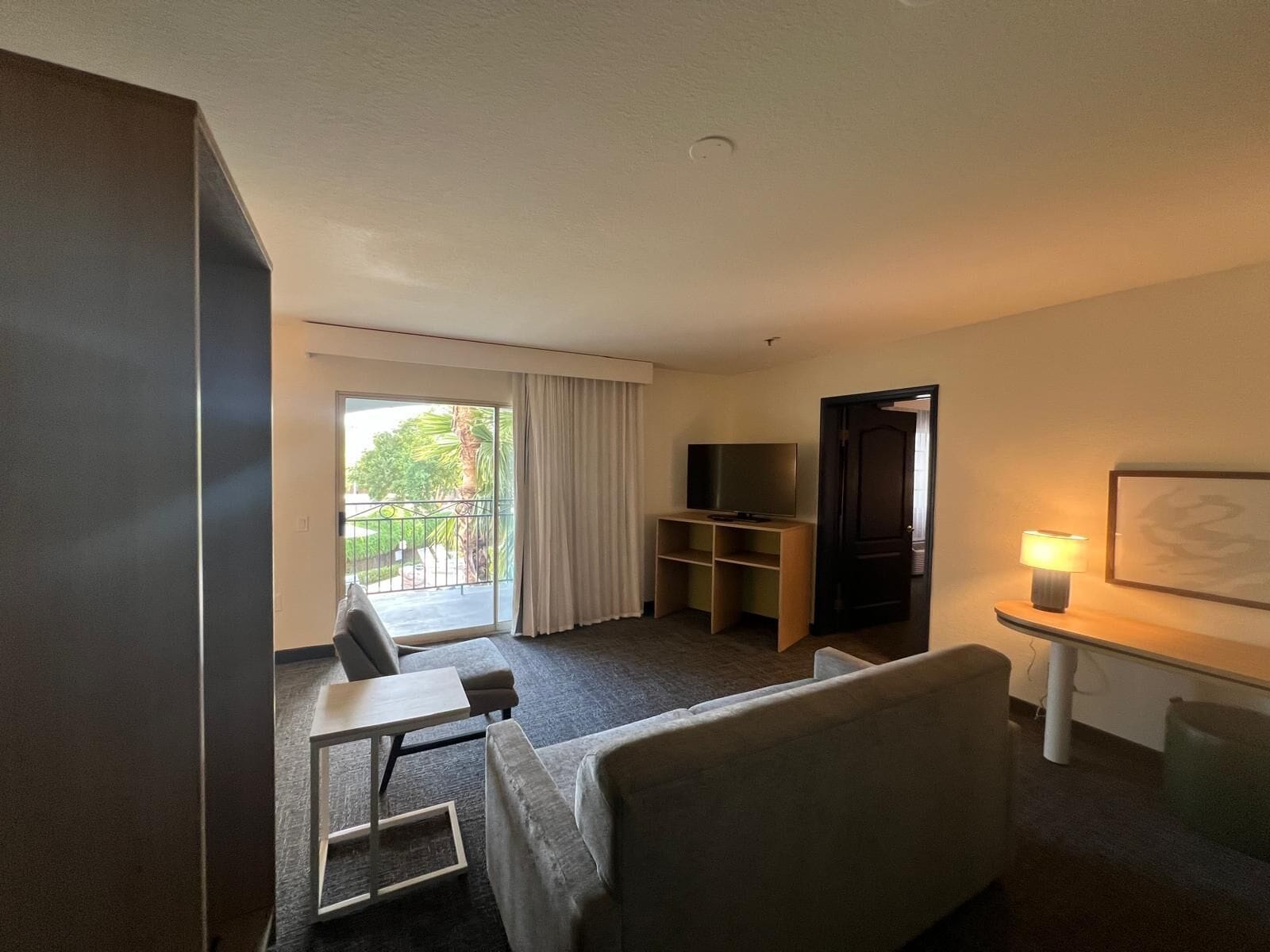 A hotel room with a balcony, a TV, a desk with a lamp, and a bed.
