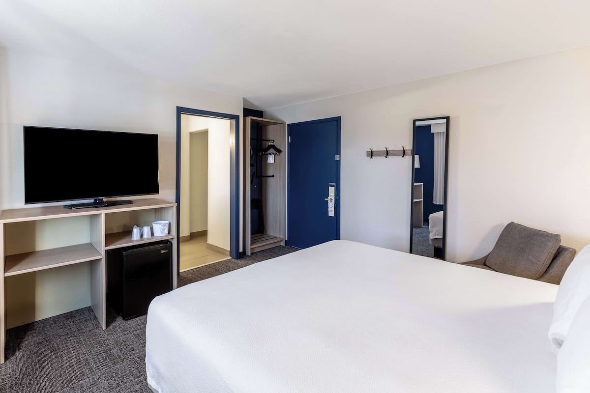 A hotel room with a bed, a TV, a desk with a computer, and a wardrobe.