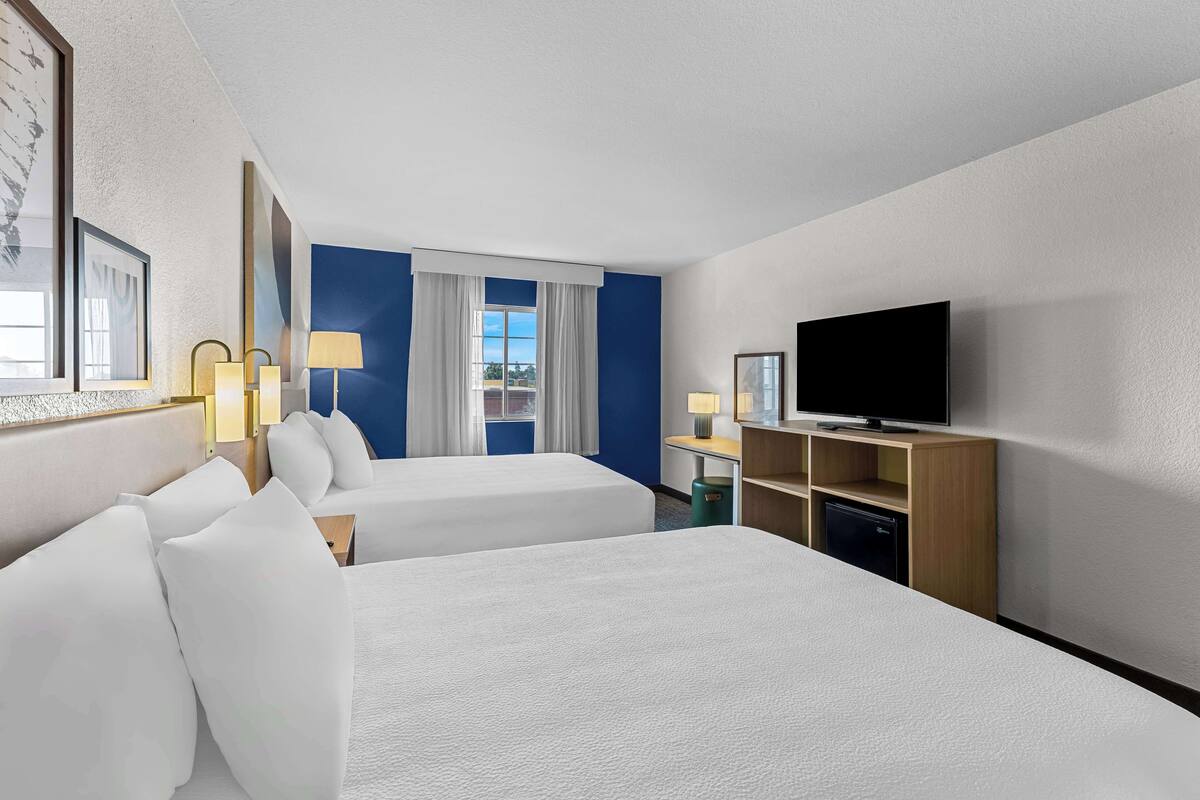 A hotel room with two beds, a television, a desk with a lamp, and a window with curtains.