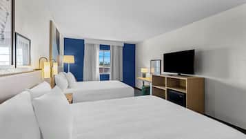 A hotel room with two beds, a television, a desk with a lamp, and a window with curtains.