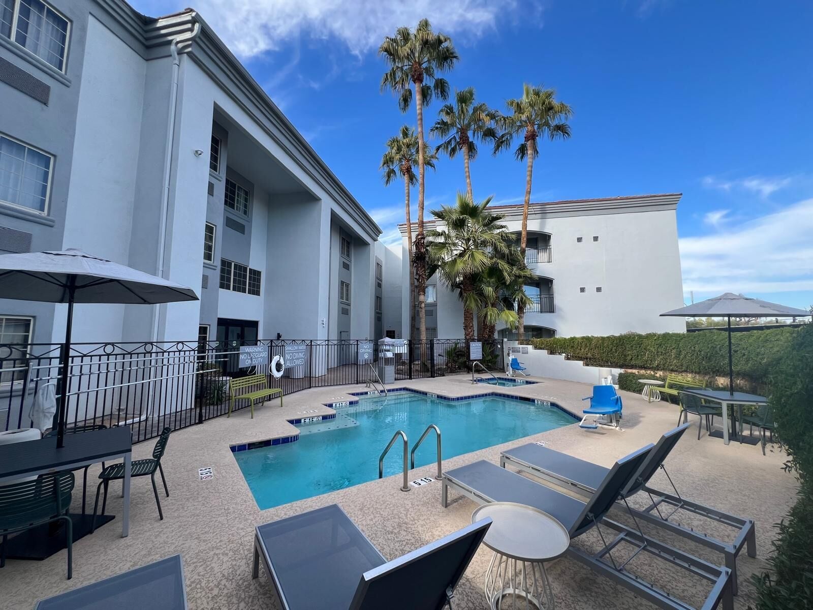A pool area with lounge chairs, umbrellas, and a building with balconies.