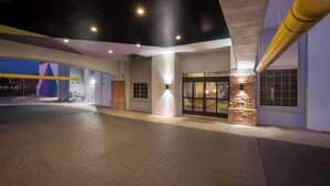 Egy modern stílusú szállodabélépő, melyet téglafal, sárga oszlop és jól megvilágított előtér jellemez.