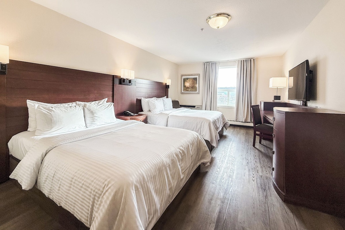 Habitación de hotel con dos camas, un escritorio, un televisor y una ventana con cortinas.