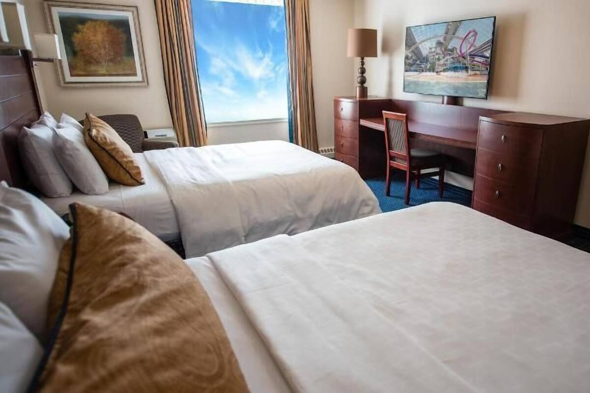 Una habitación de hotel con dos camas, un escritorio, una silla, un televisor y una puerta.