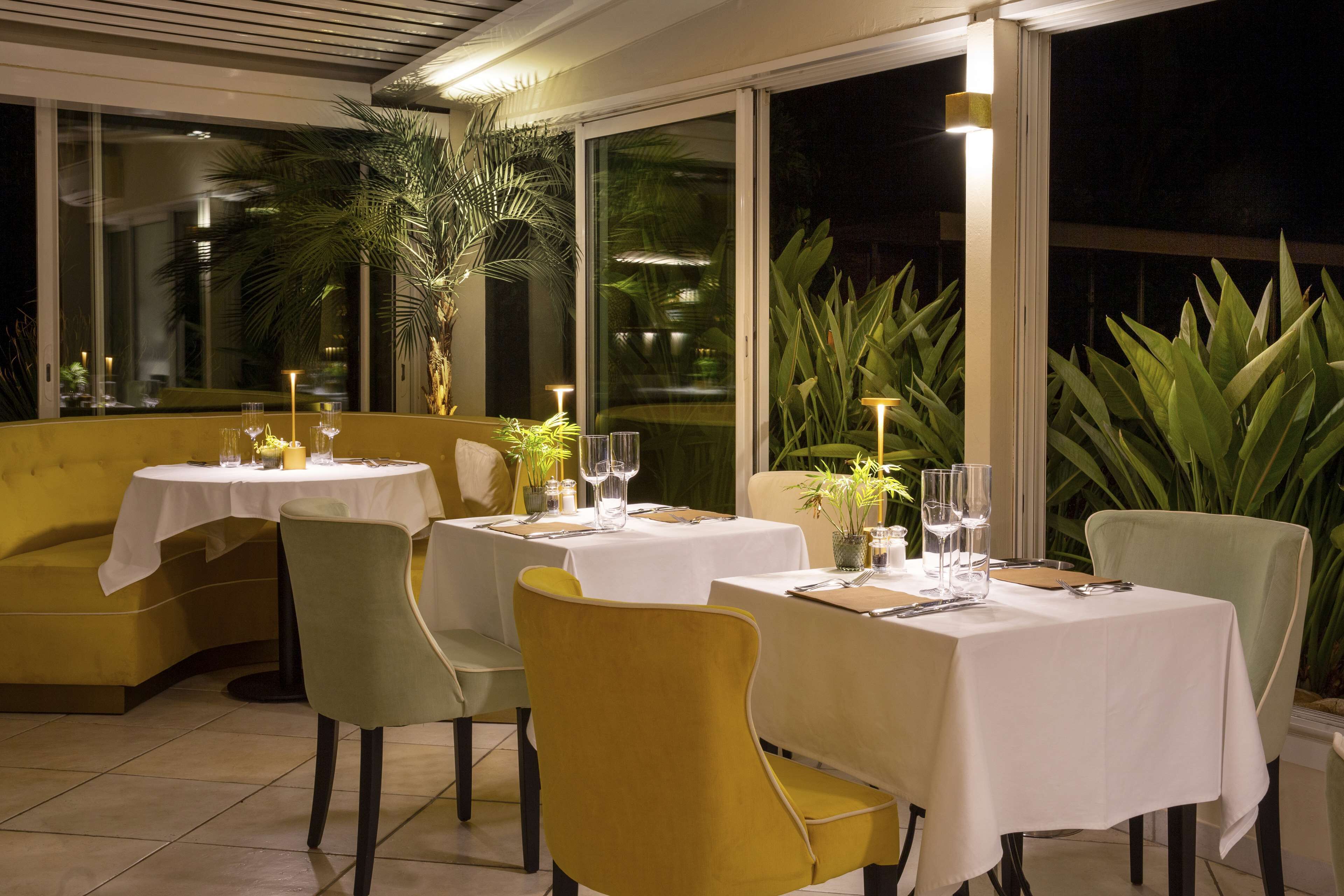 A restaurant with tables set for dining, chairs, and potted plants.