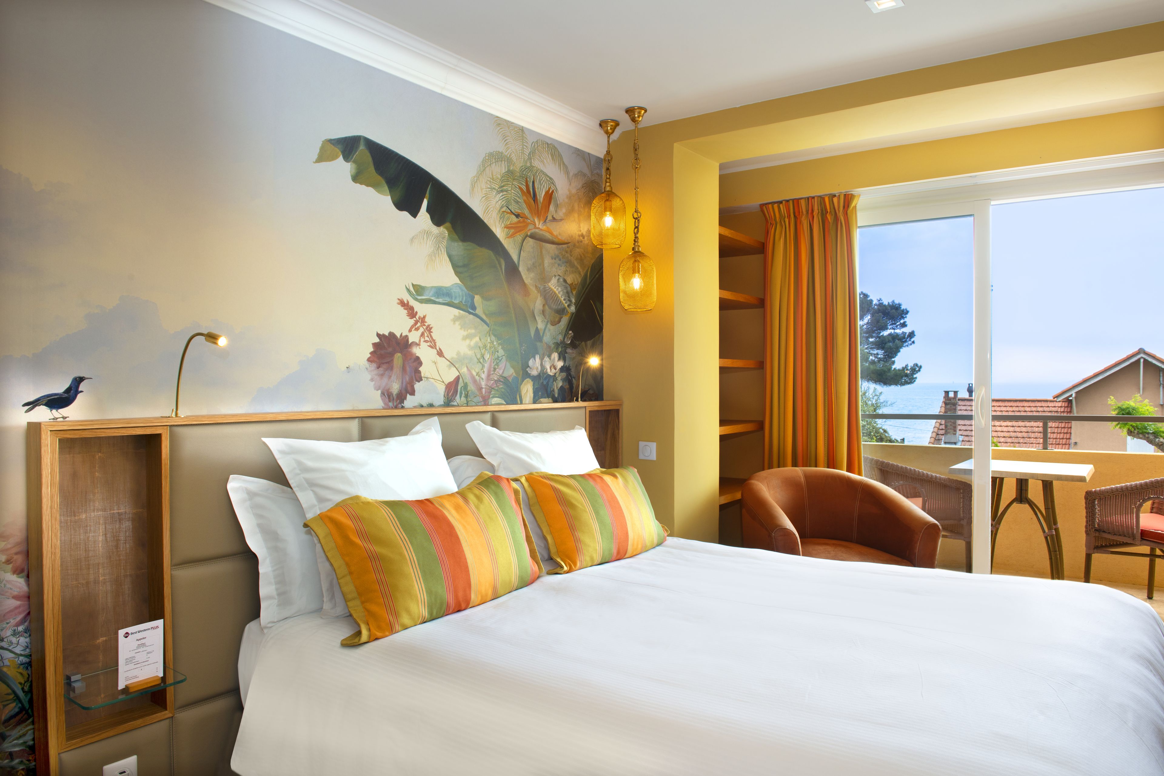 Una habitación de hotel con cama, un mural, un escritorio y vista al mar.