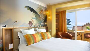 Una habitación de hotel con cama, un mural, un escritorio y vista al mar.