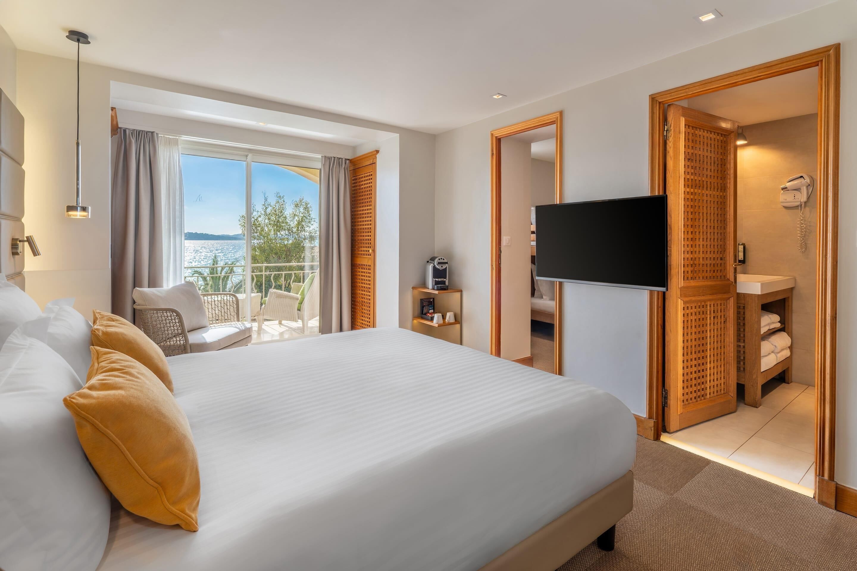 Ett hotellrum med en stor säng, en tv, en balkong med utsikt och ett badrum med en dörr av trä.