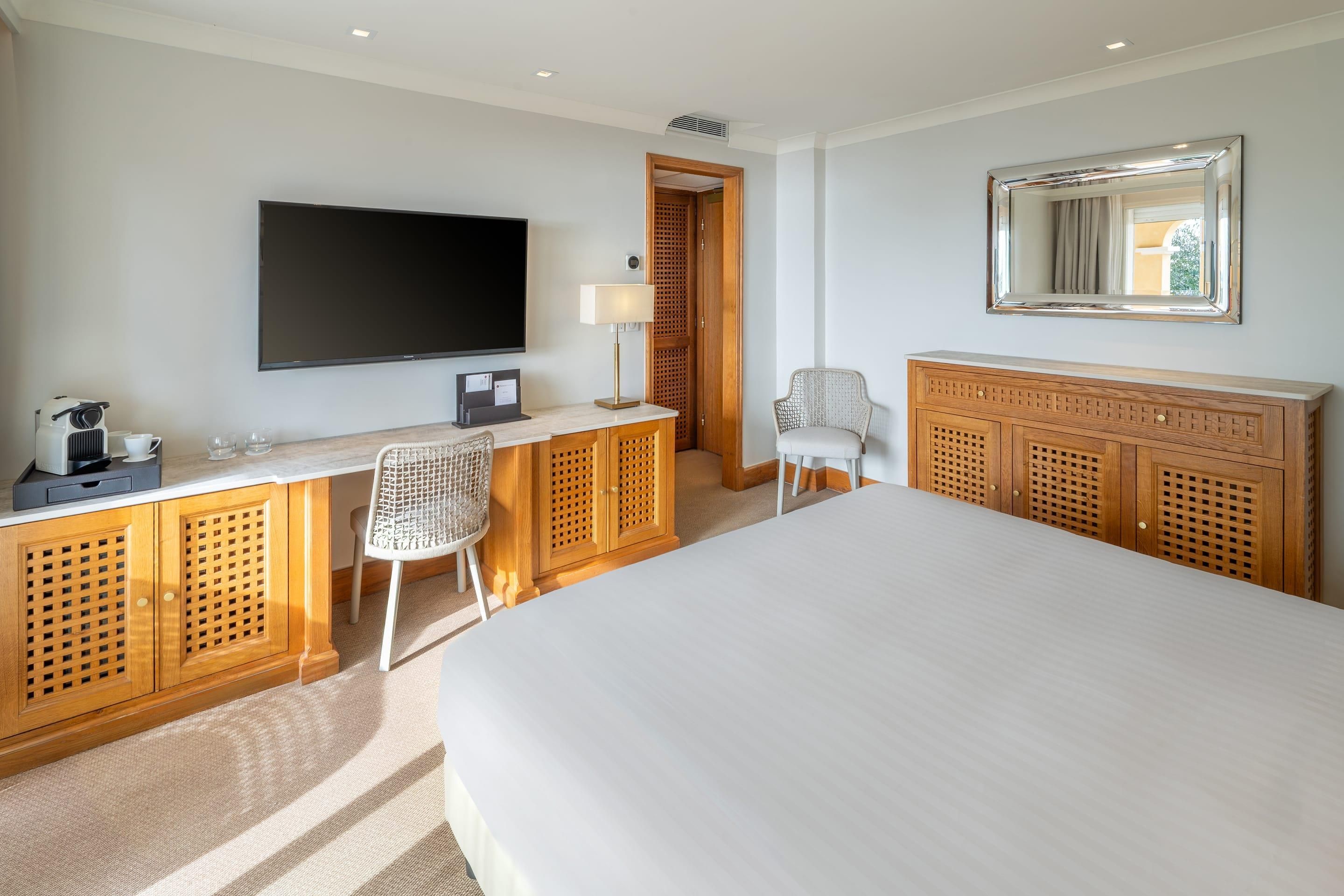 A hotel room with a large bed, a TV, a desk with a chair, and a wardrobe.