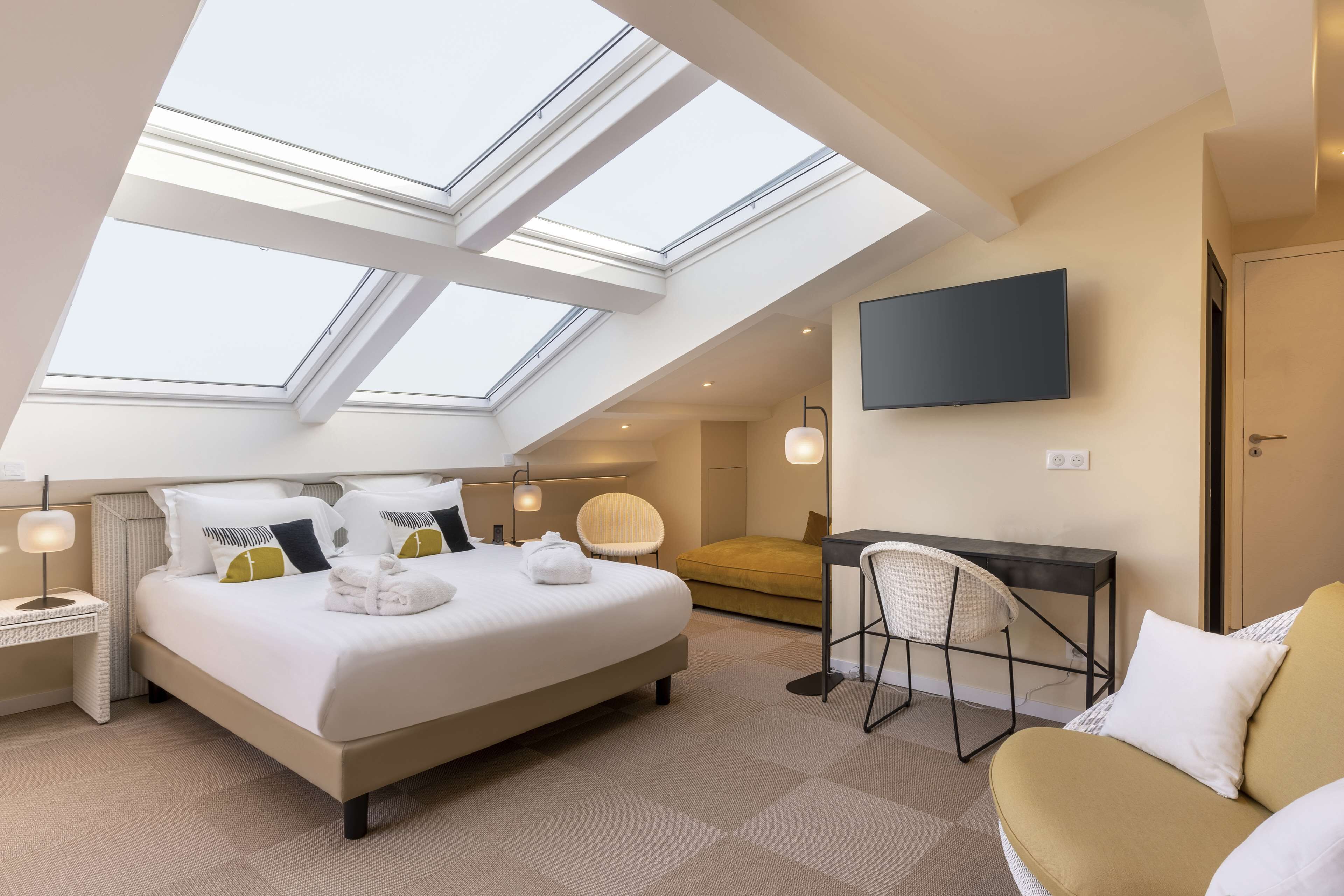 A modern hotel room with a large bed, a desk, a chair, and a TV.