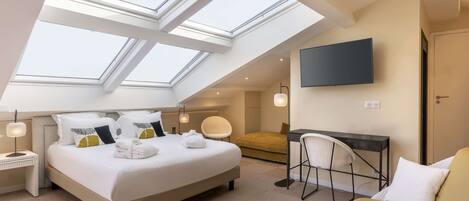 A modern hotel room with a large bed, a desk, a chair, and a TV.