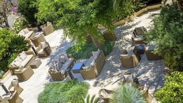 An outdoor patio area with wicker furniture, including sofas and chairs, surrounded by various plants and trees.
