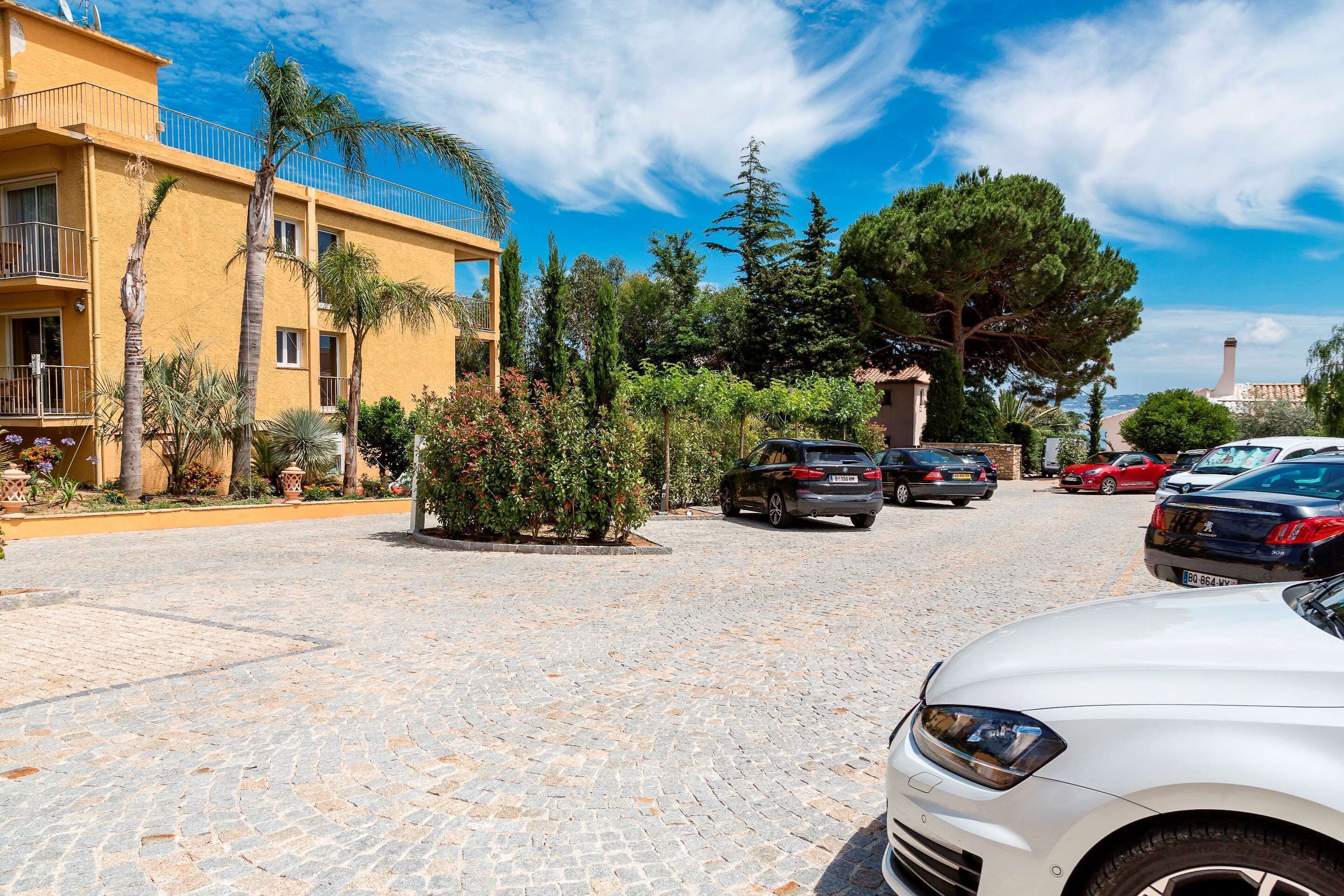 A courtyard with cobblestone pavement, a yellow building with balconies, and parked cars.